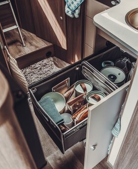 Pull-out kitchen drawer in the Carado motorhome with tableware, storage containers and extra space next to the sink