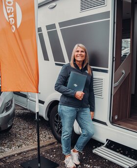 Woman standing in front of an open Carado motorhome next to a Carado flag