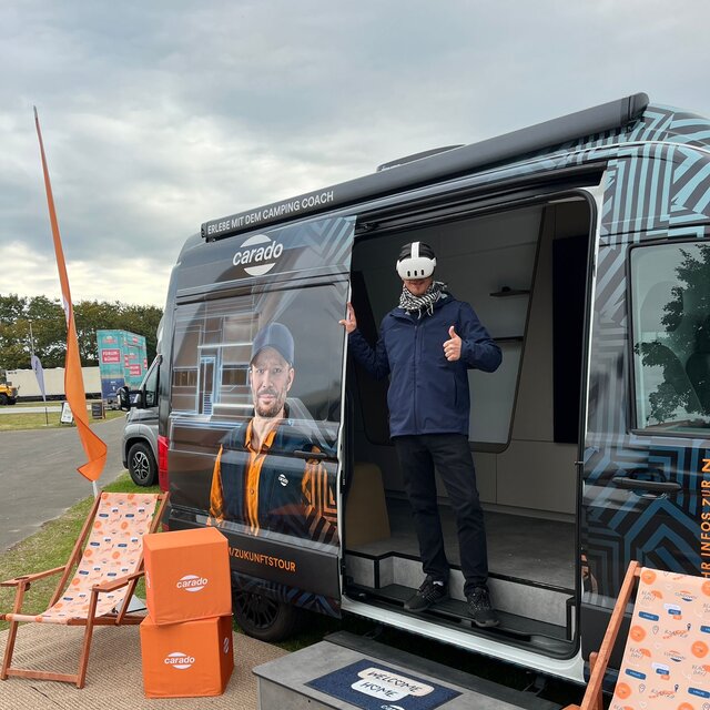 Person mit VR-Brille im Eingang eines Carado Campervan auf einer Messe