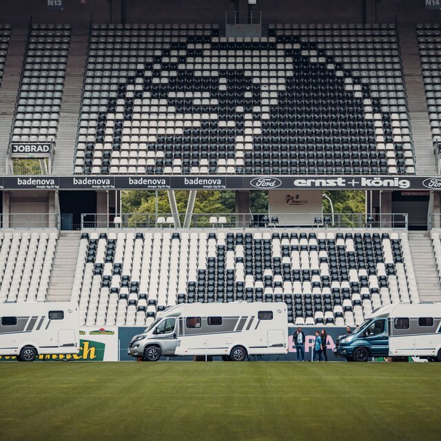 Three Carado motorhomes are parked pitchside in front of the stands of a football stadium.