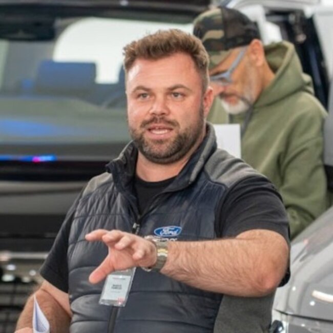 Man met microfoon en Ford-vest voor voertuigen, tweede persoon op de achtergrond