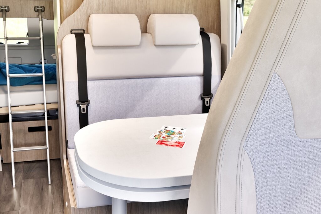 Sitzgruppe im Carado Wohnmobil mit Tisch, Gurtsitzen und Blick zum Heckbett mit Leiter