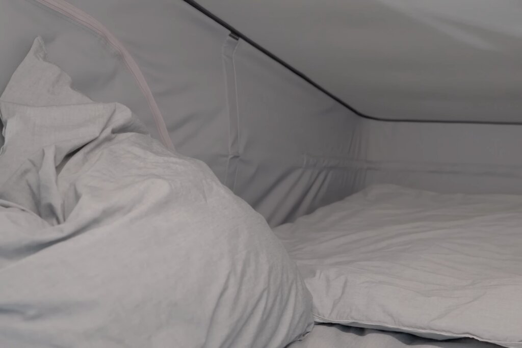 Schlafbereich im Carado Wohnmobil mit weißen Kissen und Bettdecke unter aufgeklapptem Dach