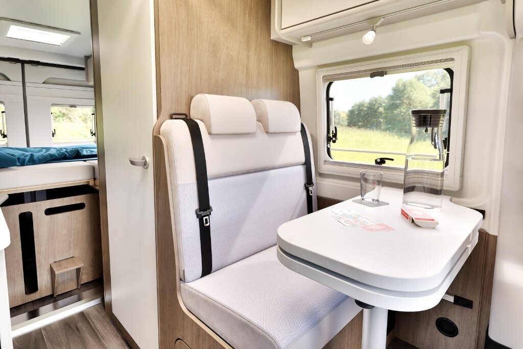Sitzgruppe im Carado Wohnmobil mit Tisch, Fenster und Blick zum Heckbett