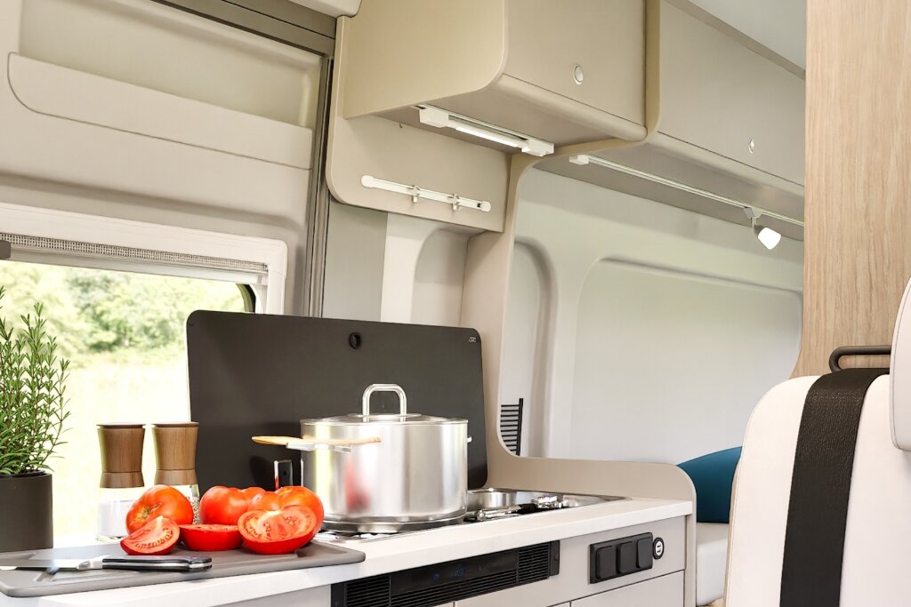 Innenraum Carado Wohnmobil mit Küchenzeile, Kochtopf auf Gasherd und Tomaten auf Schneidebrett