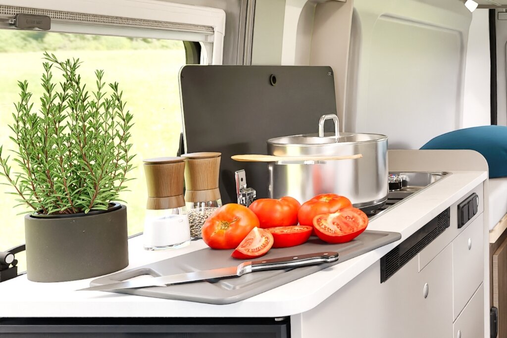 Küche im Carado Wohnmobil mit Kochtopf, Tomaten, Messer und Gewürzmühlen auf der Arbeitsfläche