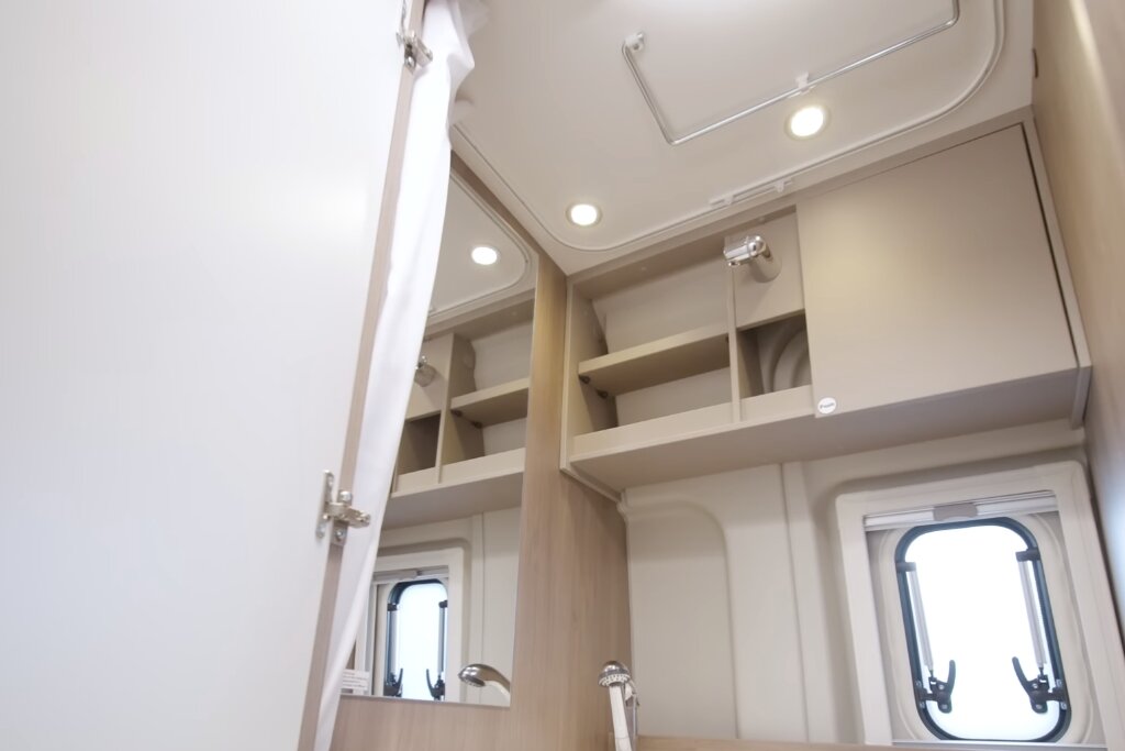 Bad im Carado Wohnmobil mit Spiegelschrank, offenen Ablagen, Dachhaube und seitlichem Fenster
