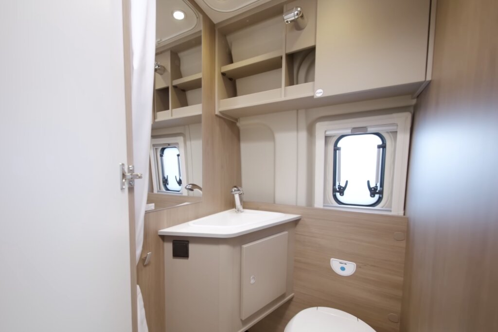 Badezimmer im Carado Wohnmobil mit Waschbecken, Spiegel, Toilette, Fenster und offenen Oberschränken