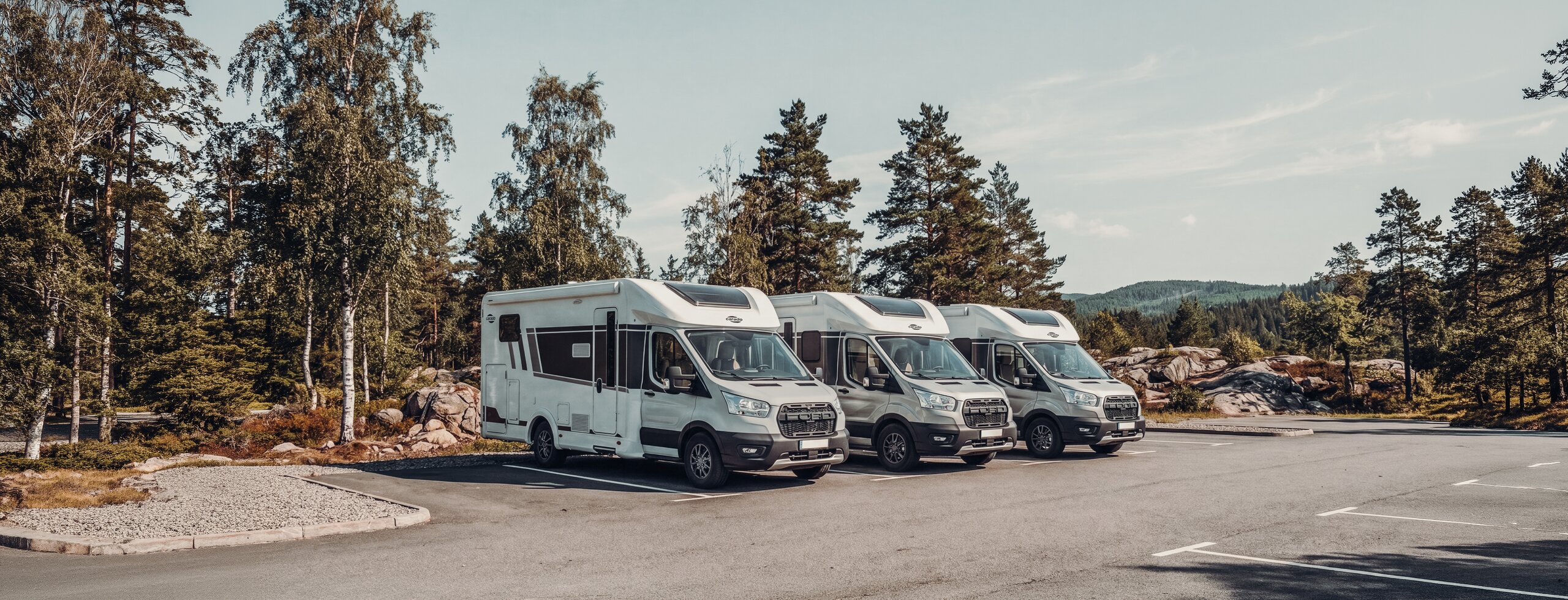 Drie Carado campers geparkeerd aan de bosrand, van voren en van opzij gezien