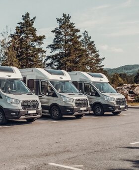 Drie Carado campers in zijaanzicht geparkeerd op een parkeerplaats voor de bomen