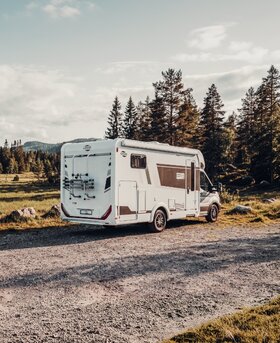 Carado T 338 halfintegraal camper op een grindpad aan de bosrand, achter- en zijaanzicht