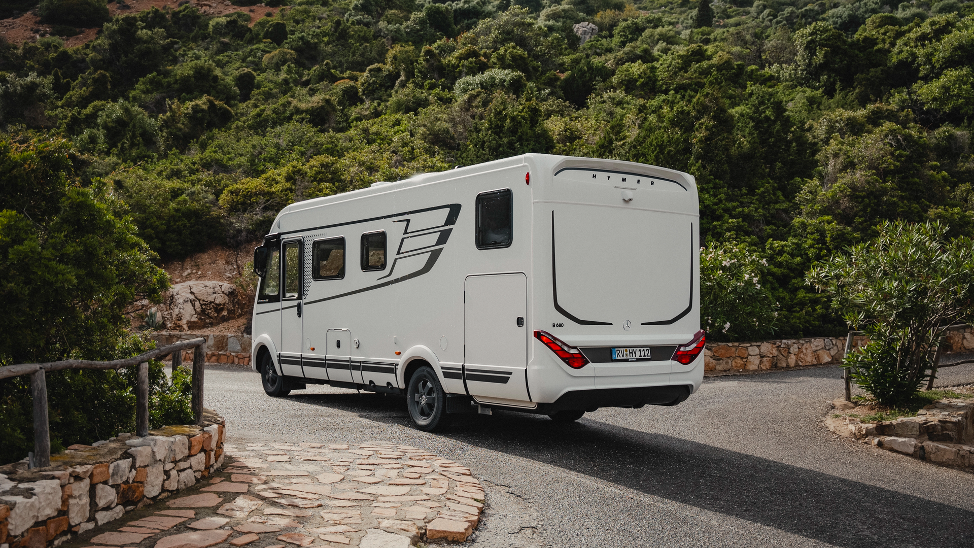 Hymer B‑MC I in dynamischer Heckansicht auf einer kurvenreichen Panoramastraße mit markantem LED‑Heckdesign und mediterraner Bergkulisse