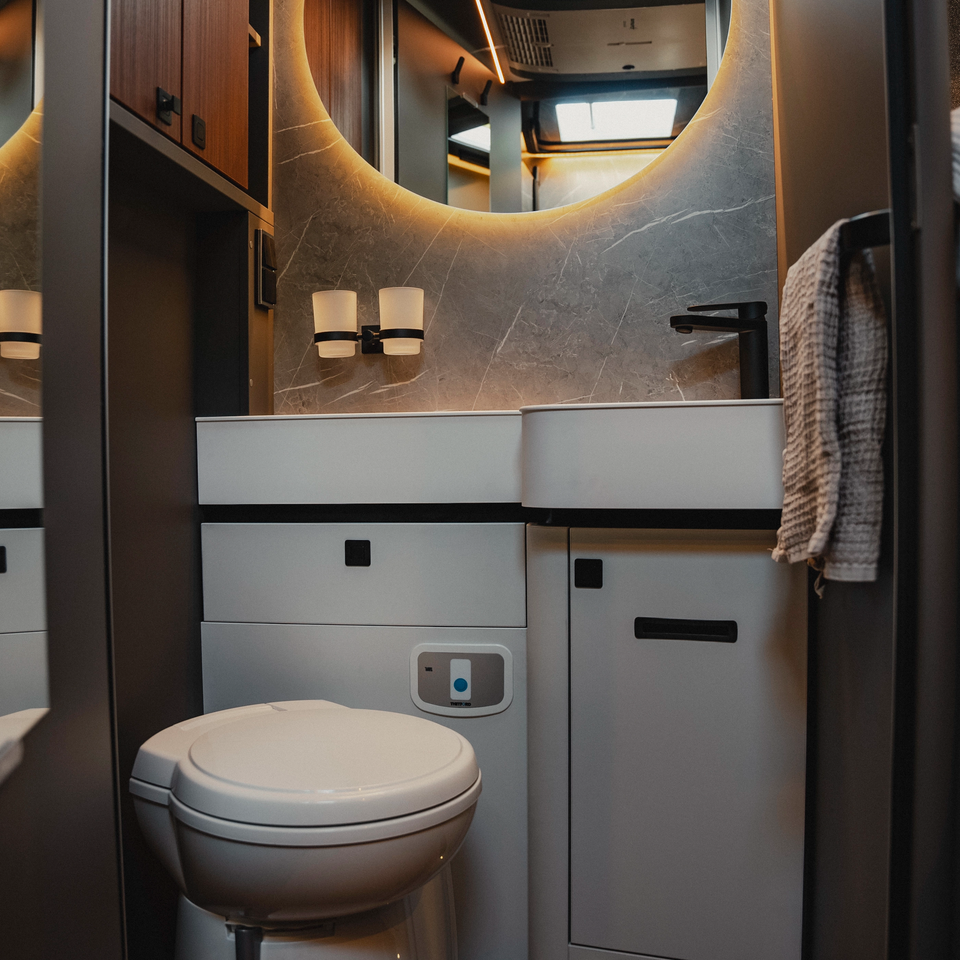 Modernes Badezimmer im Hymer B‑MC I mit beleuchtetem Rundspiegel, hochwertigem Waschtisch, WC und durchdachtem Stauraumkonzept für komfortables Reisen