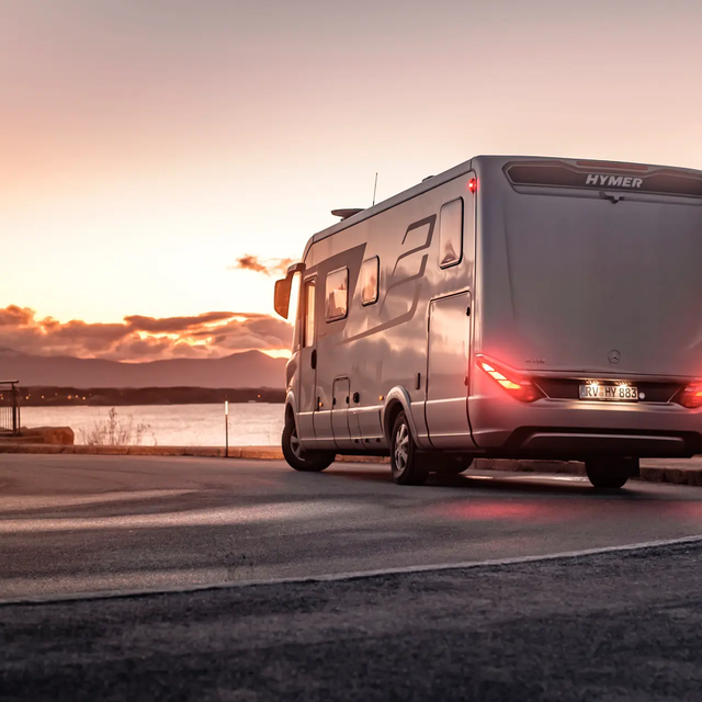 in Kurve fahrende HYMER B-Klasse MasterLine I an skandinavischer Küste im Sonnenuntergang