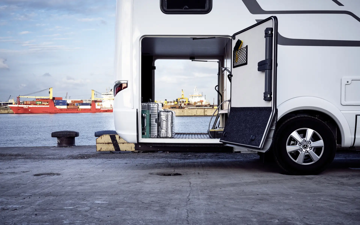 Blick durch die mit silbernen Koffern beladene Heckgarage der HYMER B-Klasse MasterLine vor Hafenanlage mit rotem Frachter