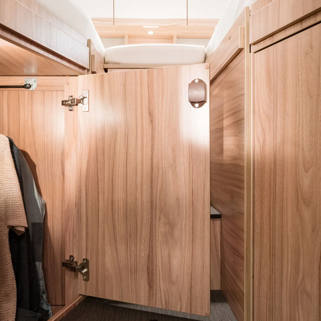 Mit Oberteilen an der Stange befüllter und beleuchteter Kleiderschrank unterm Längseinzelbett beim HYMER Exsis-t