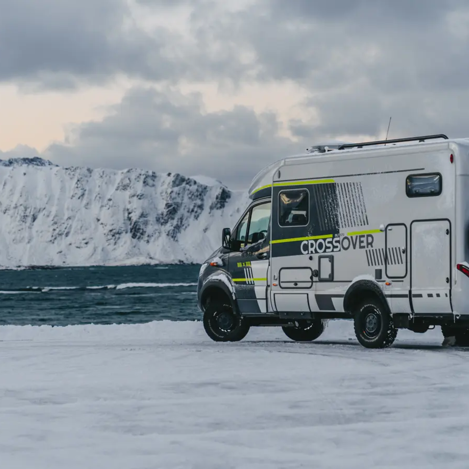 Sideutsikt av HYMER ML-T 570 CrossOver, høyt snødekt fjell og havet i bakgrunnen