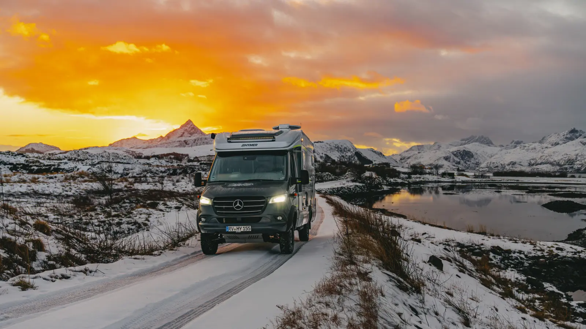 HYMER ML-T 570 kjører på veien, snødekte fjell og en vakker solnedgang i bakgrunnen