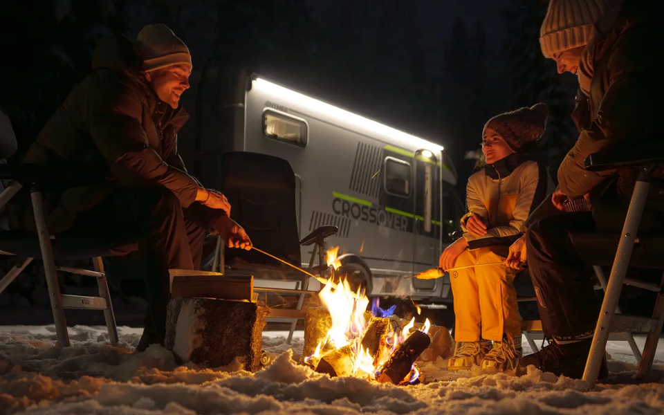 3 personer sitter ved et leirbål og lager pinnebrød, HYMER ML-T 570 CrossOver i bakgrunnen